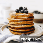 Stack of whole wheat pancakes on a white plate topped with fresh blueberries and a sprinkle of powdered sugar.