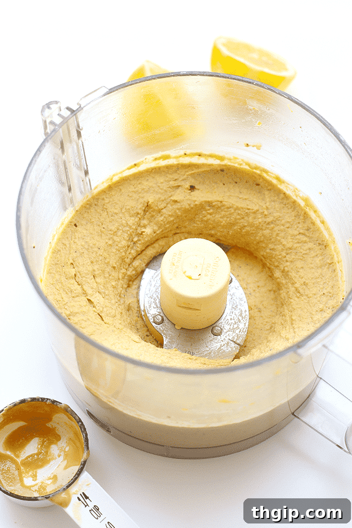 Zesty Lemon Hemp Hummus 3 Close-up shot of perfectly blended lemon hemp hummus inside a food processor, showcasing its creamy and smooth texture.