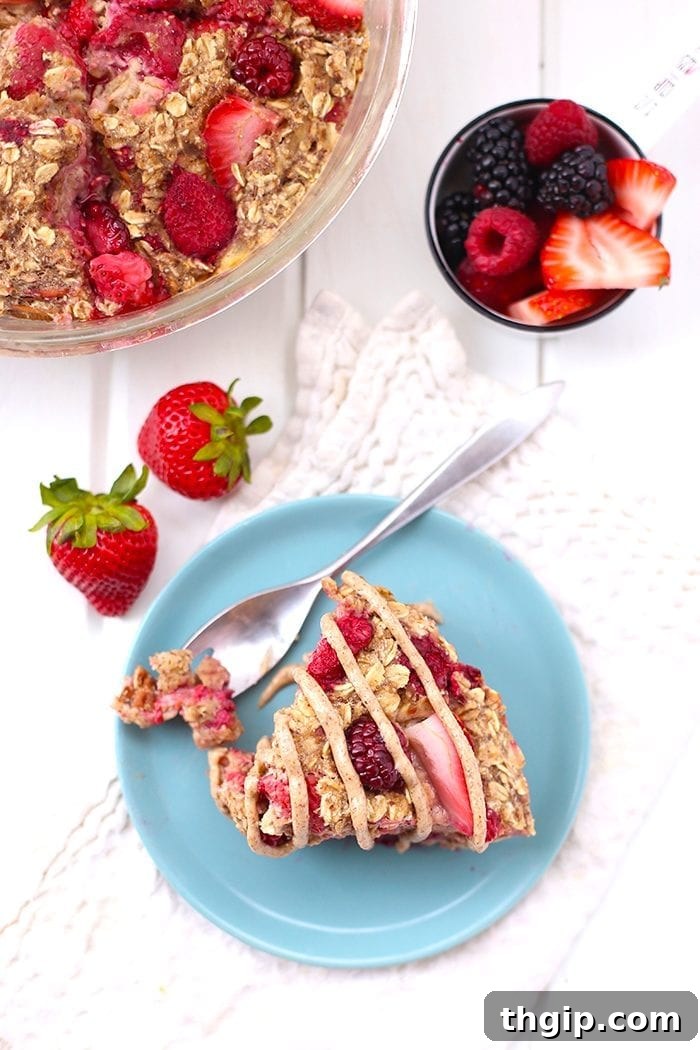 Berry Burst Baked Oatmeal 4 A slice of Triple Berry Baked Oatmeal on a plate with additional fresh berries and a drizzle of maple syrup, illustrating a tempting serving suggestion.
