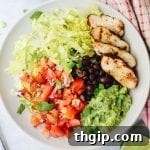 A vibrant homemade Chipotle Burrito Bowl, brimming with fresh ingredients like chicken, rice, beans, salsa, guacamole, and lettuce.