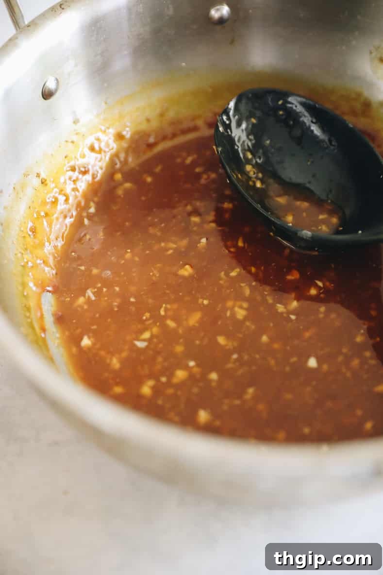 Caramelized Orange Chicken 5 Sticky orange chicken sauce cooking in saucepan with black spoon sitting inside.