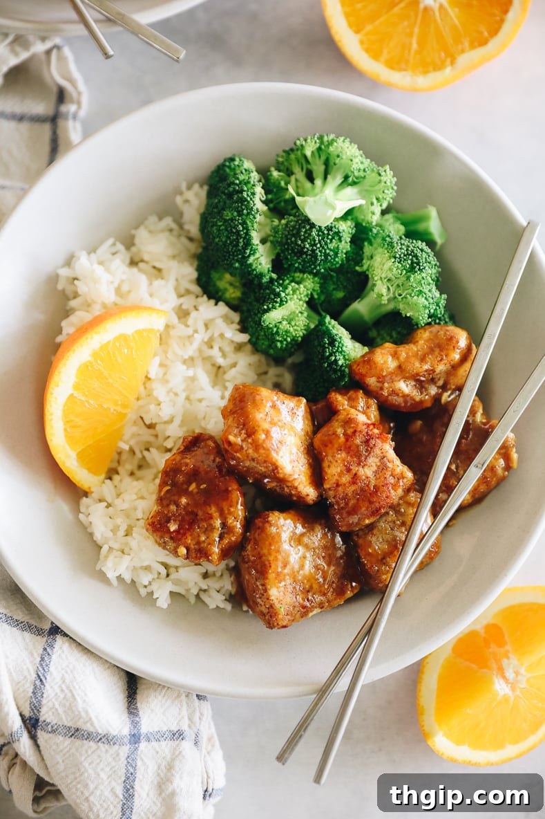 Caramelized Orange Chicken 10 Sticky orange chicken on a white plate with rice and broccoli. Silver chopsticks crossed on top.