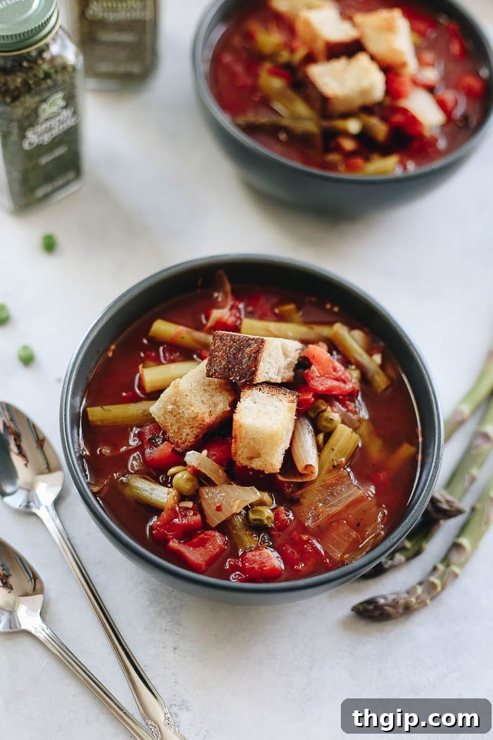 Vibrant Spring Harvest Soup 2 A comforting bowl of vibrant Spring Vegetable Soup, generously topped with golden, homemade garlicky croutons, surrounded by fresh asparagus spears and fragrant herbs, evoking a sense of seasonal freshness.