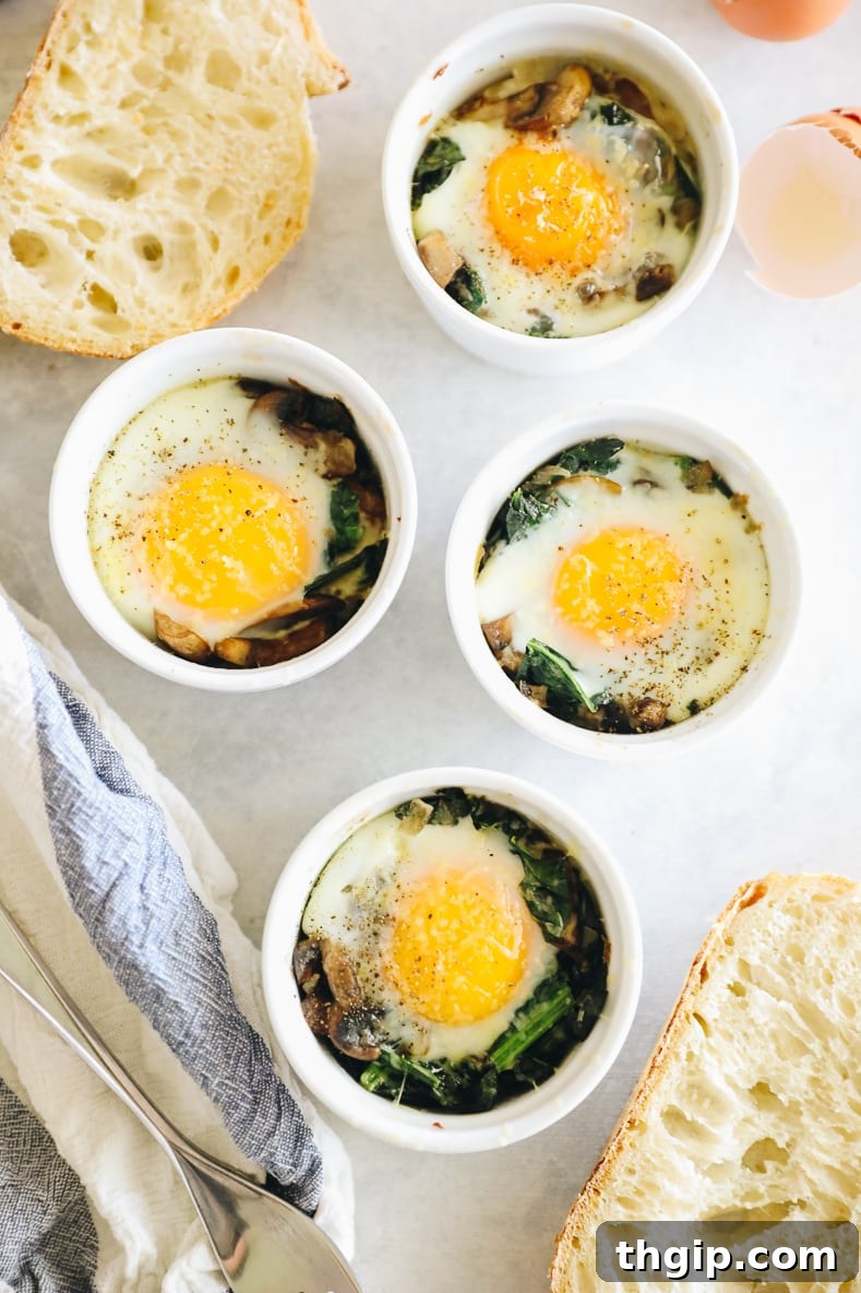 Shirred Eggs 7 An overhead shot showcasing four beautifully baked eggs in ramekins, surrounded by golden-brown sourdough bread slices.