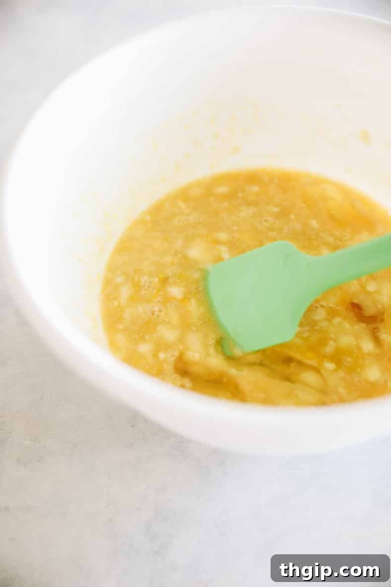 Wholesome Zucchini Banana Bread 5 Wet ingredients including mashed bananas, maple syrup, and eggs mixed in a separate bowl.