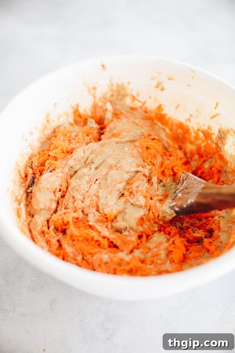 Wet ingredients with grated carrot, apple, walnuts, and raisins mixed in a bowl.