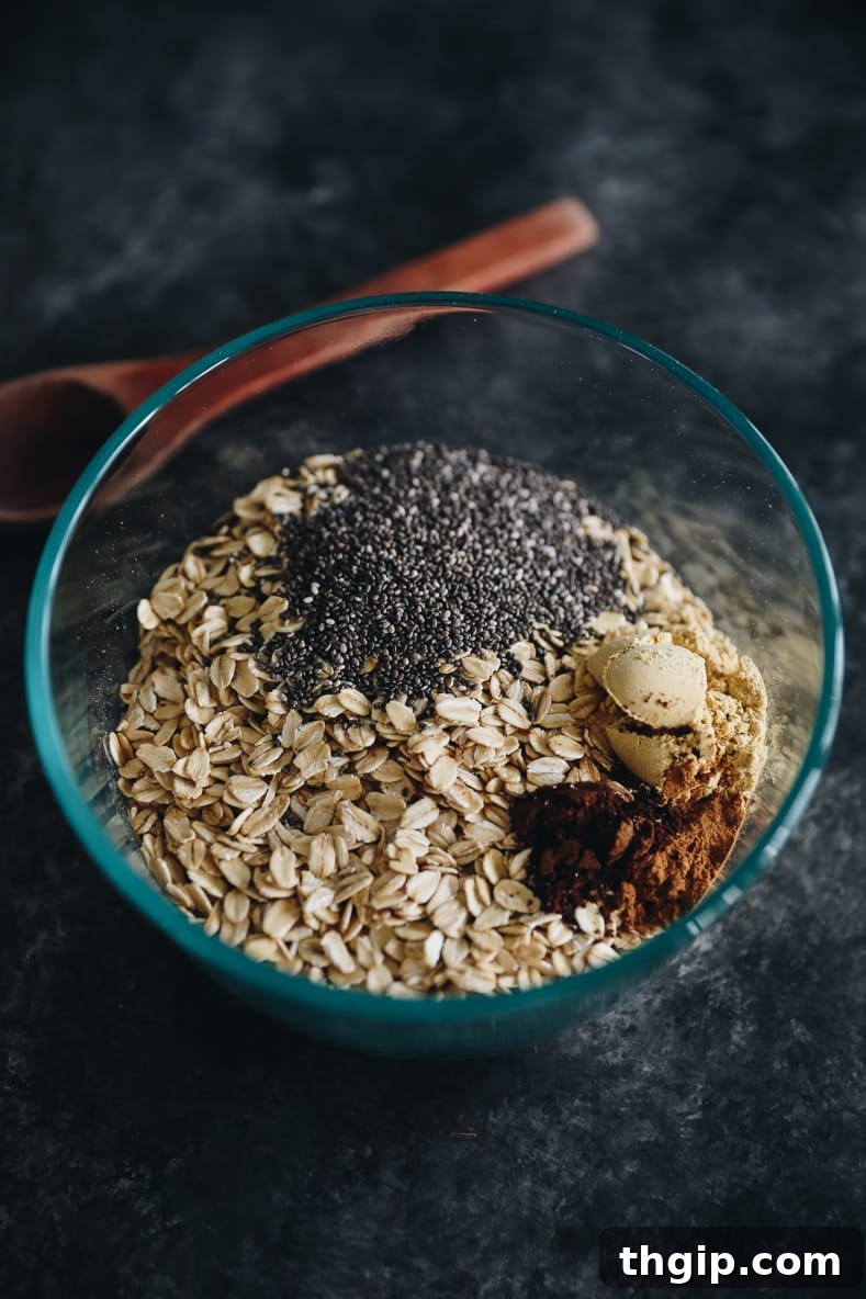 Cozy Gingerbread Overnight Oats 3 Dry ingredients of gingerbread overnight oats in a clear bowl. Wooden mixing spoon in the background.