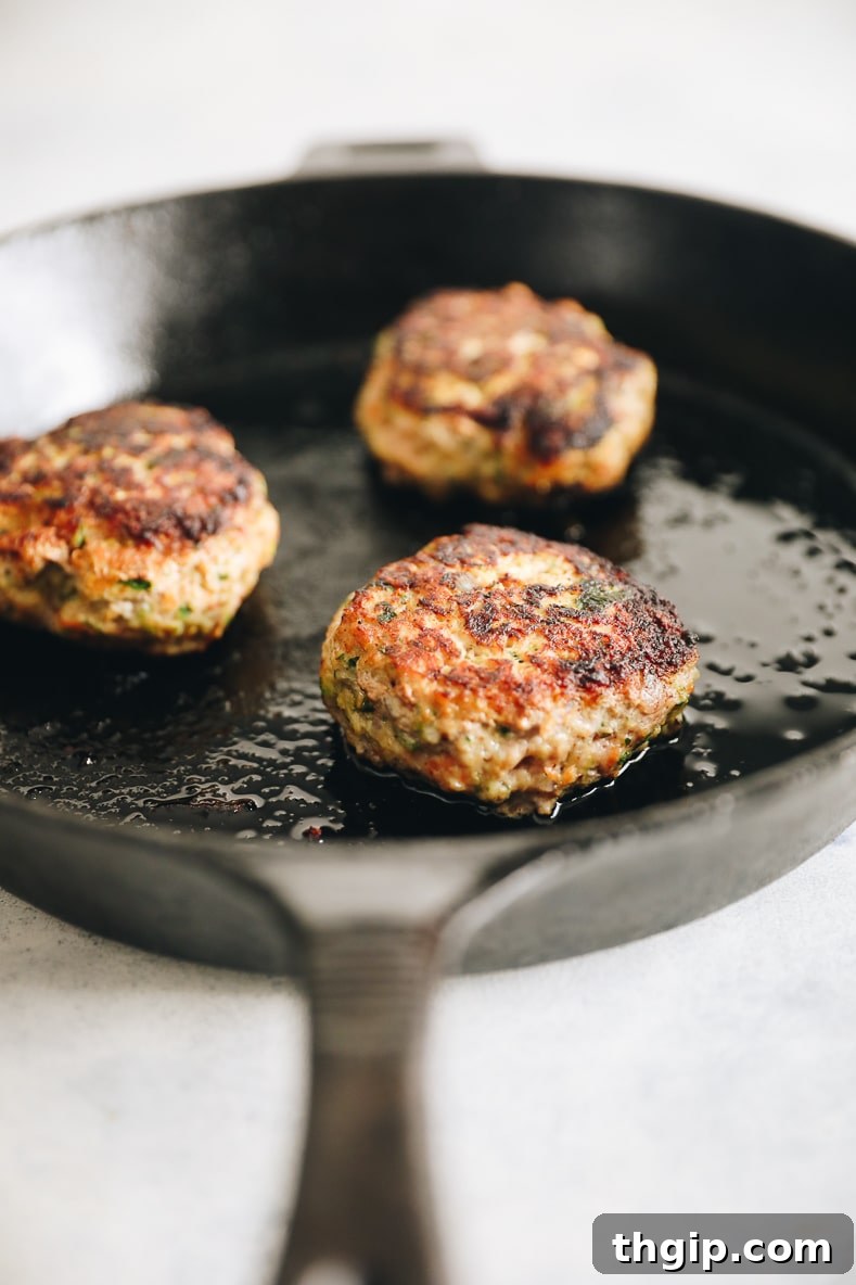 Zesty Thai Turkey Burgers with Peanut Drizzle 5 Turkey burger patties cooking in a hot skillet, achieving a golden-brown crust.