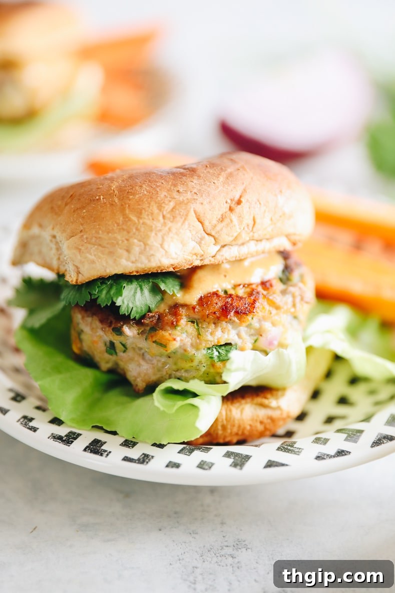 Zesty Thai Turkey Burgers with Peanut Drizzle 7 A close-up of a cooked Thai Turkey Burger patty with peanut sauce, fresh cilantro, and a slice of lime on a wooden board.