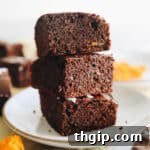 Three decadent sweet potato brownies stacked on a pristine white plate, garnished with a sprinkle of cocoa powder.