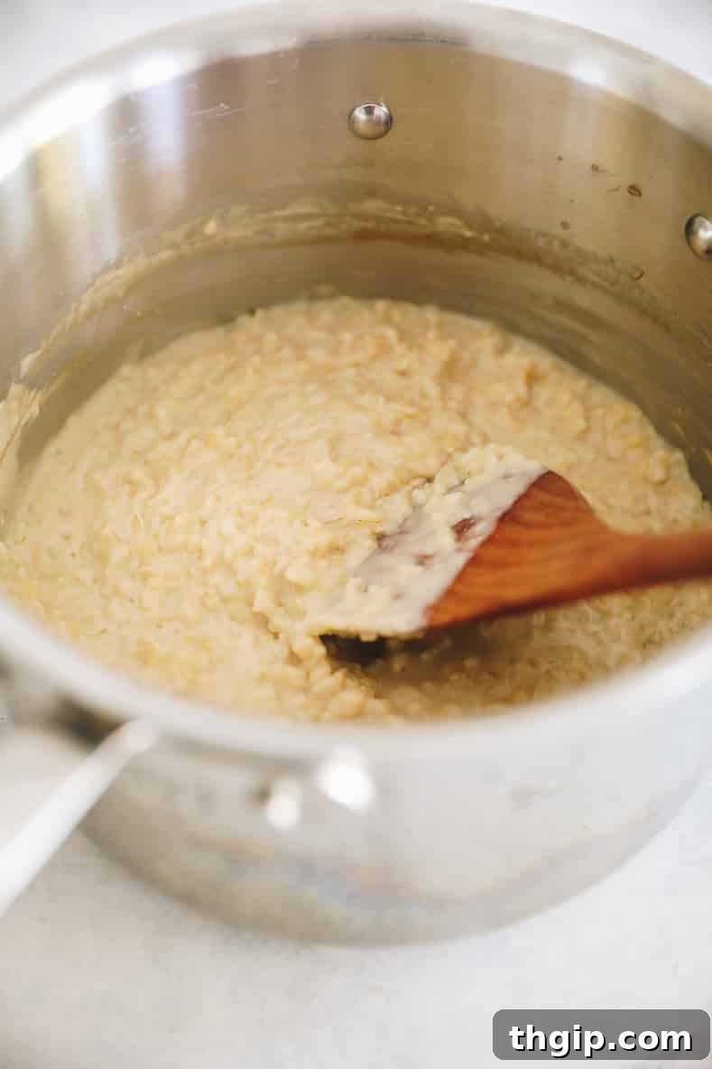 Rice pudding mixture in metal pot with wooden spoon stirring.