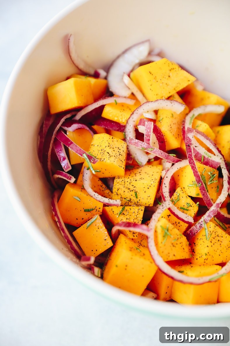 Roasted Rosemary Butternut Squash 3 Butternut squash cubes, red onion slices, and fresh rosemary sprigs in a mixing bowl, tossed with olive oil, ready for roasting.