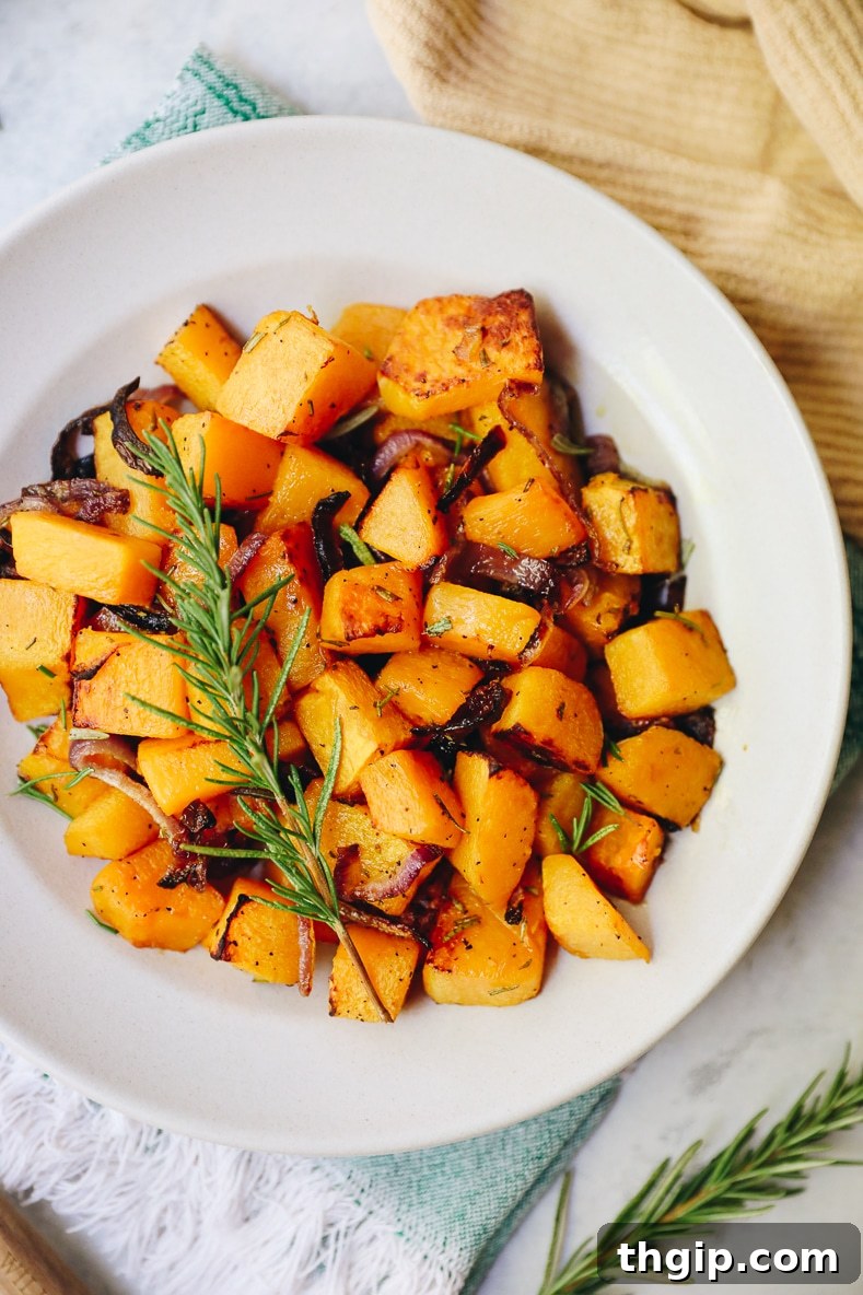 Roasted Rosemary Butternut Squash 7 A wide shot of the roasted rosemary butternut squash in a white bowl, ready to be served, with hints of red onion and green rosemary.