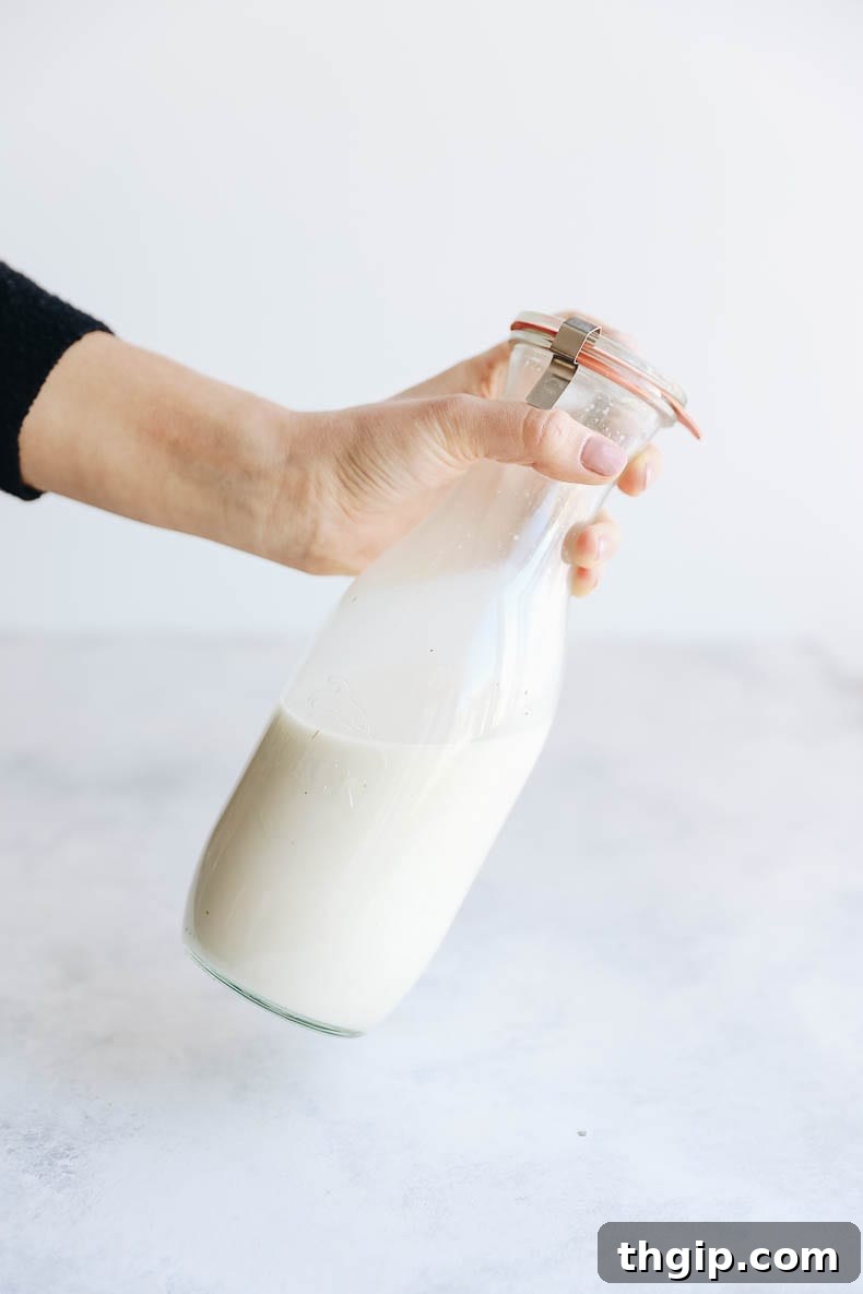 Make Your Own Oat Milk 5 Hand holding a glass jar filled with freshly made homemade oat milk, ready for storage.