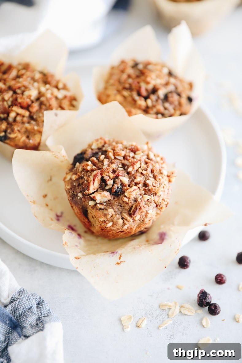 Bursting Blueberry Oat Muffins 2 Freshly baked blueberry oatmeal muffins with a golden pecan streusel topping, cooling in a muffin tin.