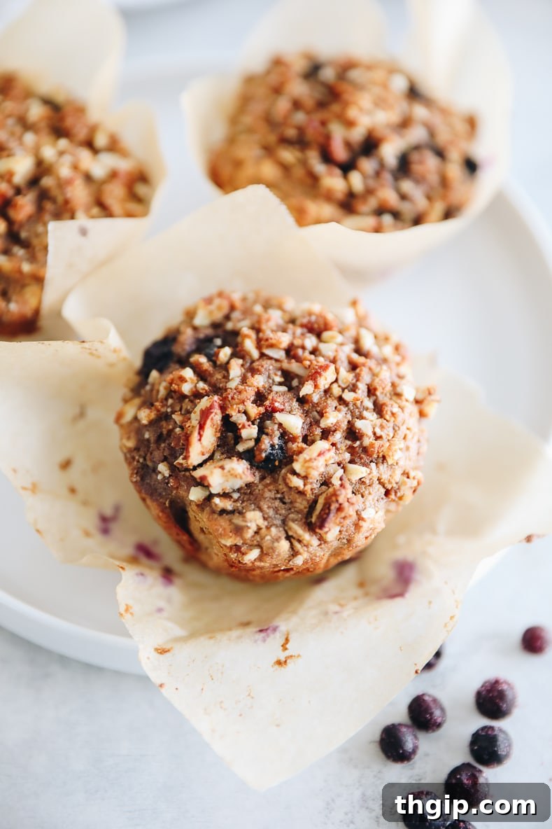 Bursting Blueberry Oat Muffins 9 Close up of a blueberry oat muffin on a white plate with a paper muffin tin, showing its texture.
