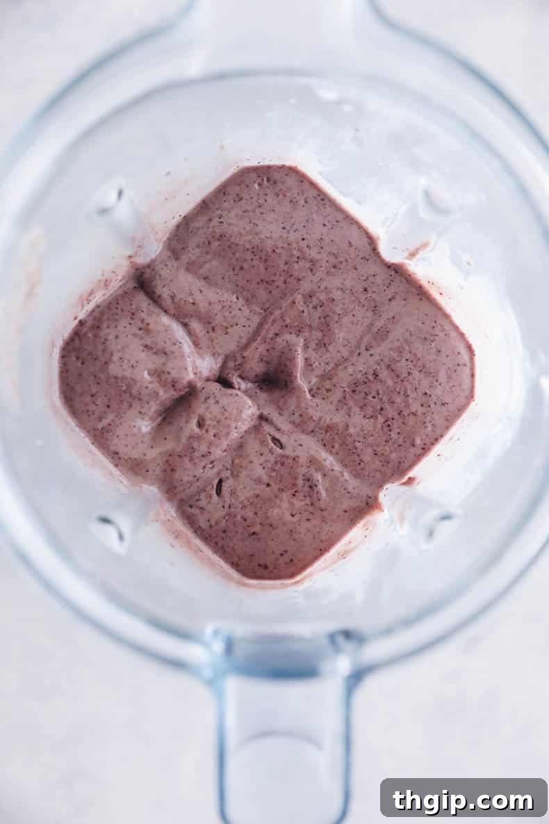 Blender filled with ingredients for a blueberry smoothie, including frozen blueberries, spinach, and avocado, ready to be blended.