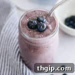 Delicious blueberry superfood smoothie in a mason jar, topped with fresh berries and a metal straw.