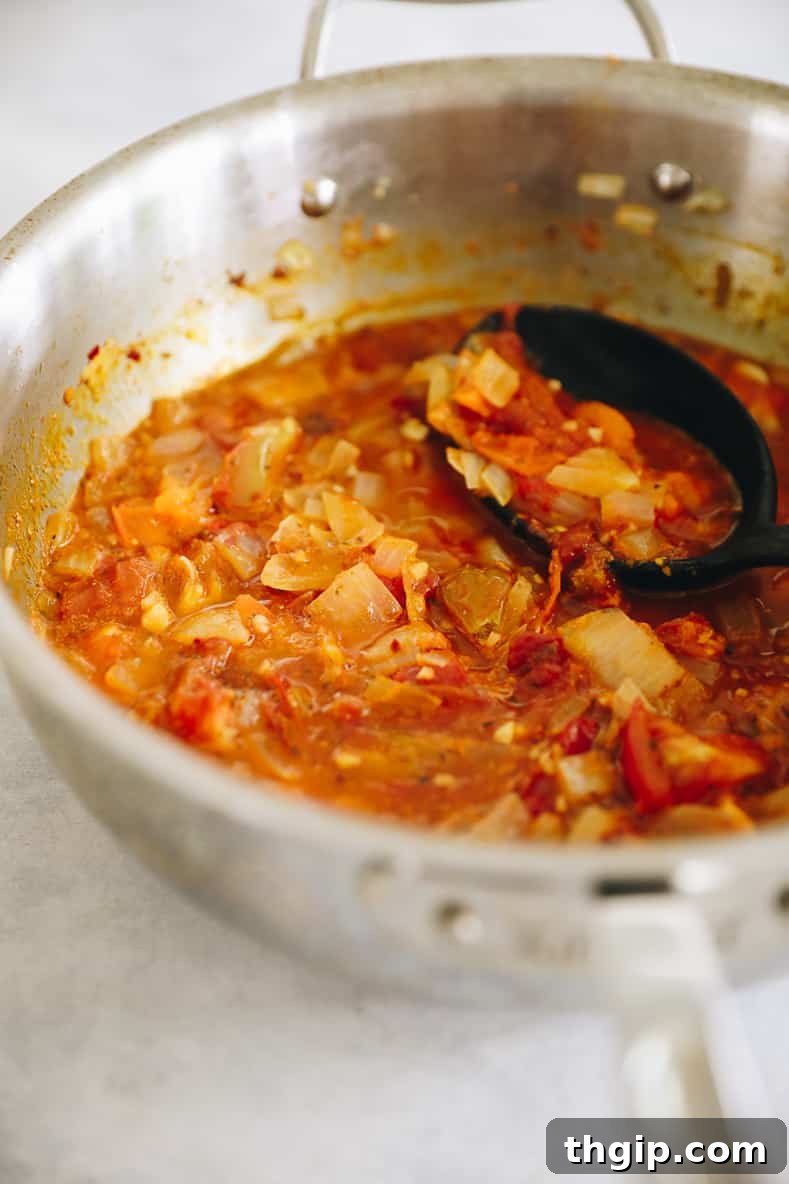 Fiery Homemade Arrabbiata 3 Cooking tomatoes, onions and garlic in a large pot to make homemade arrabbiata sauce, showing the ingredients bubbling.
