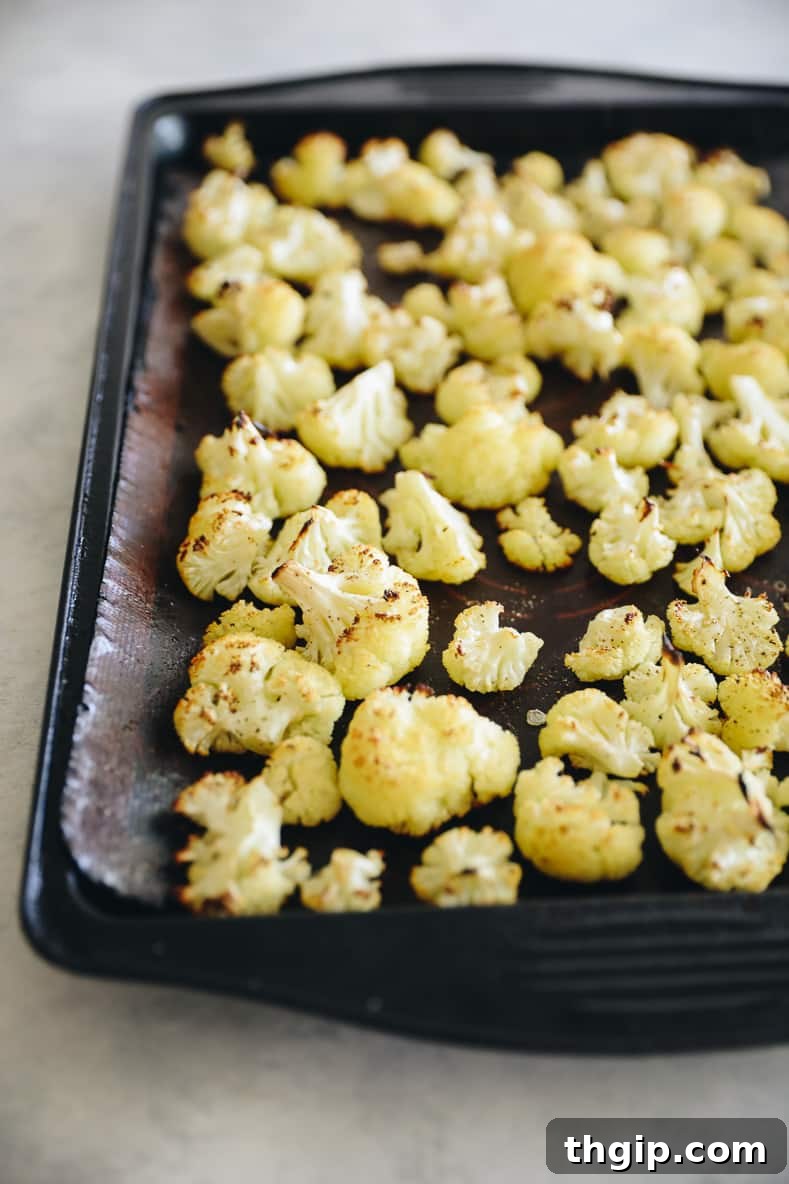 Mediterranean Roasted Cauliflower and Chickpeas with Tahini Za'atar 3 Cauliflower florets seasoned with olive oil, salt, and pepper spread in a single layer on a parchment-lined baking sheet, ready for roasting.
