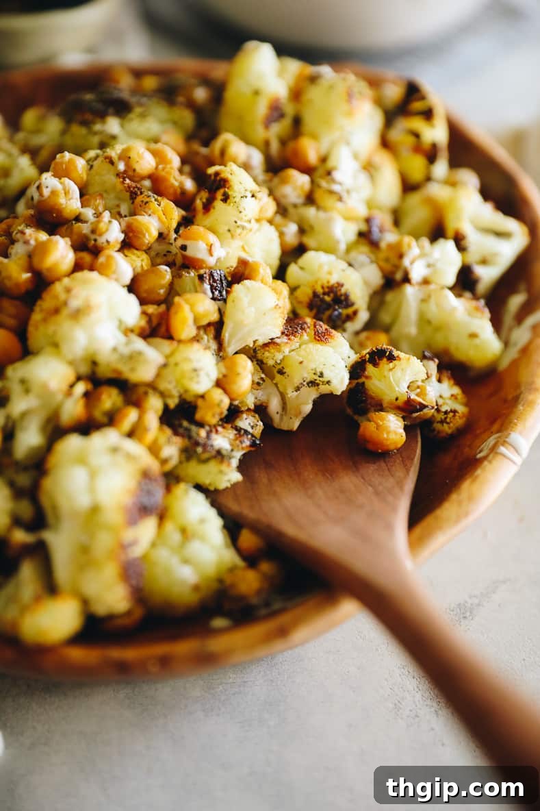 Mediterranean Roasted Cauliflower and Chickpeas with Tahini Za'atar 6 A beautiful wooden serving bowl brimming with roasted cauliflower and golden-brown chickpeas, artfully drizzled with creamy tahini sauce and sprinkled with za'atar. A wooden spoon rests invitingly on the side of the bowl.