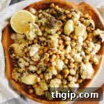 An overhead shot of a wooden serving bowl filled with roasted cauliflower and chickpeas, perfectly dressed and seasoned.