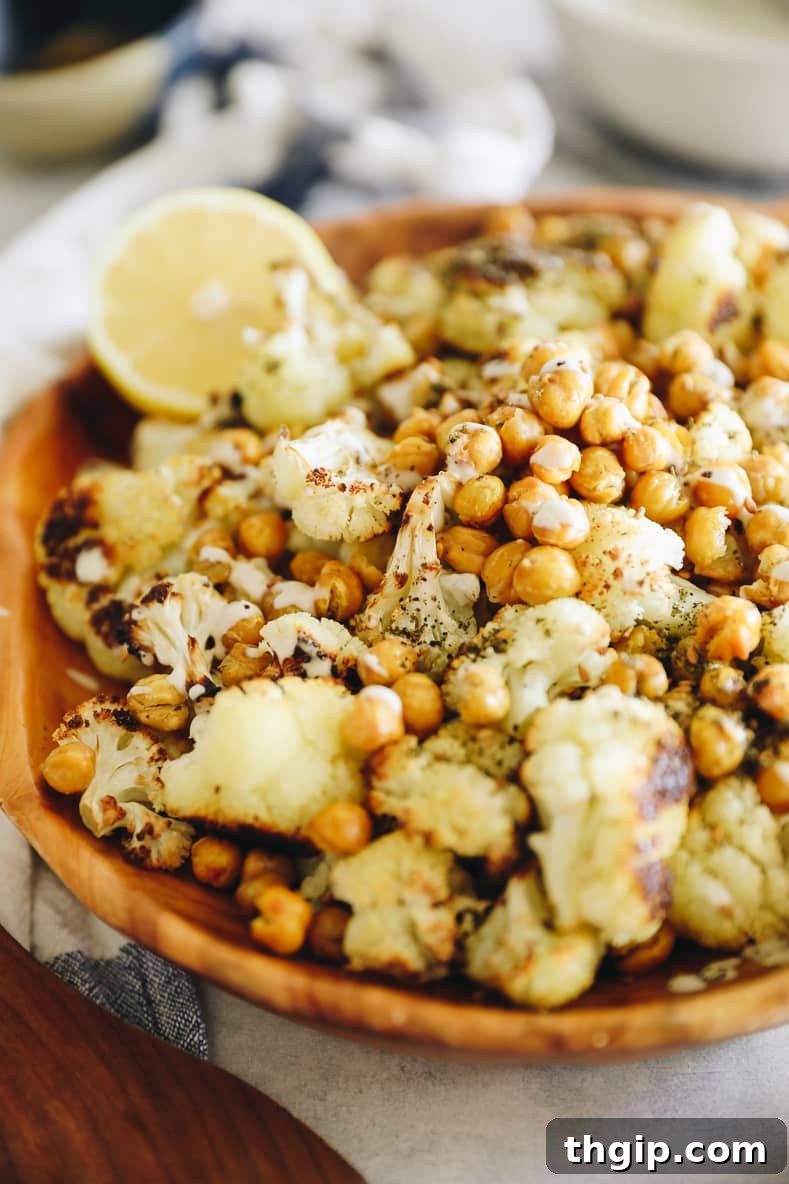 Mediterranean Roasted Cauliflower and Chickpeas with Tahini Za'atar 7 A wooden serving bowl filled with roasted cauliflower and chickpeas, with a wooden spoon resting on the side. The dish is beautifully presented, highlighting its texture and color.