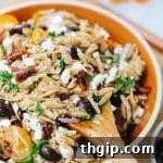 A close-up shot of a bowl of Mediterranean Orzo Salad, with fresh ingredients visible.