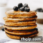 Stack of whole wheat pancakes on a white plate topped with fresh blueberries and a sprinkle of powdered sugar.