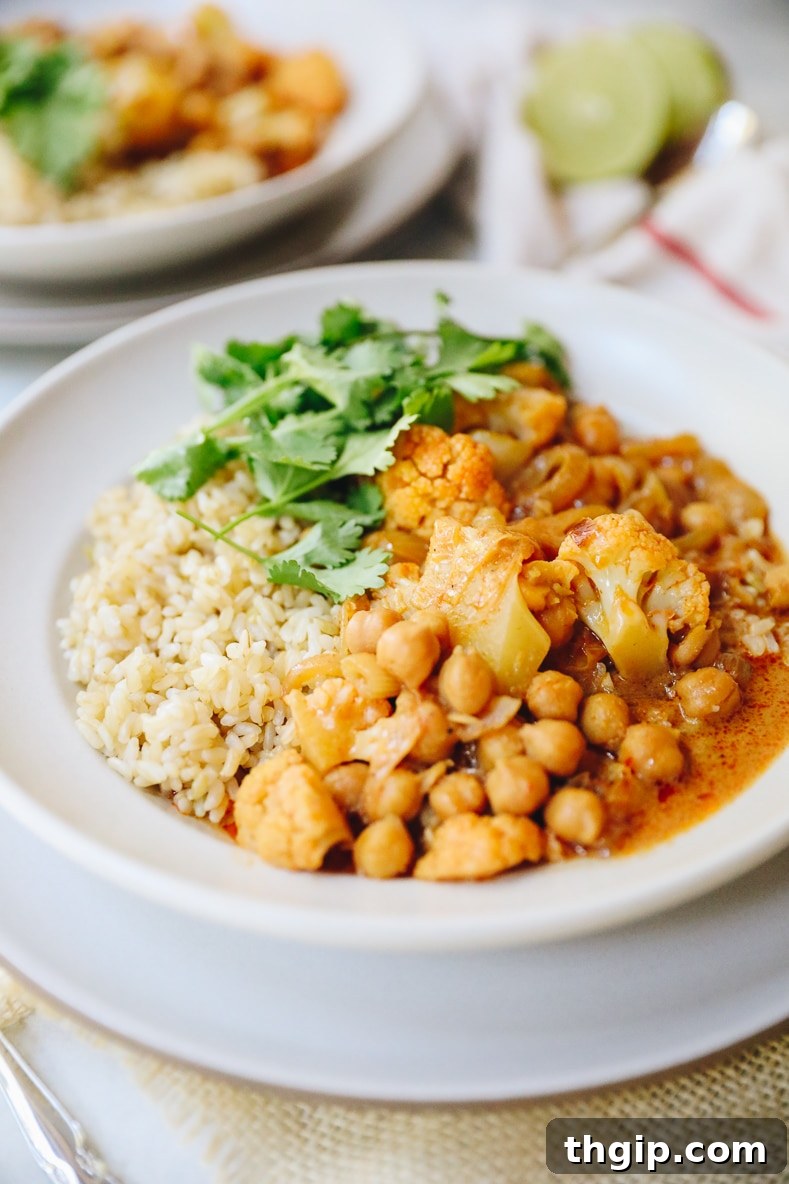 A vibrant bowl of cauliflower and chickpea Massaman curry, garnished with fresh cilantro and crushed peanuts, served alongside fluffy white rice.