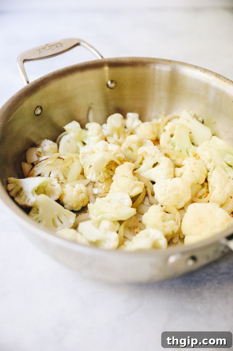 Sliced onions and minced garlic are sautéed in coconut oil in a large pan.