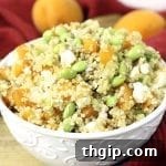 Vibrant Apricot & Edamame Quinoa Salad in a white bowl with a spoon, garnished with fresh apricots and green onions.