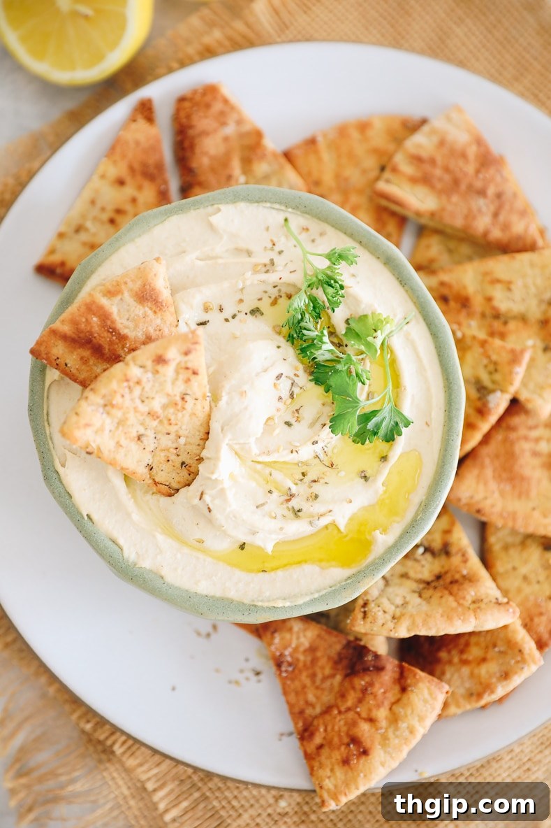 Dreamy Creamy Hummus 2 A vibrant green bowl filled with creamy homemade hummus, surrounded by golden pita chips, ready to be enjoyed.