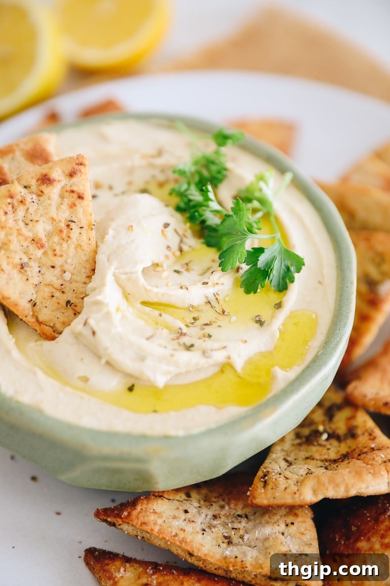 Dreamy Creamy Hummus 3 A close-up view of velvety smooth hummus, beautifully garnished with a swirl of olive oil, a sprinkle of vibrant za'atar, and fresh parsley, presented in a stylish green bowl.
