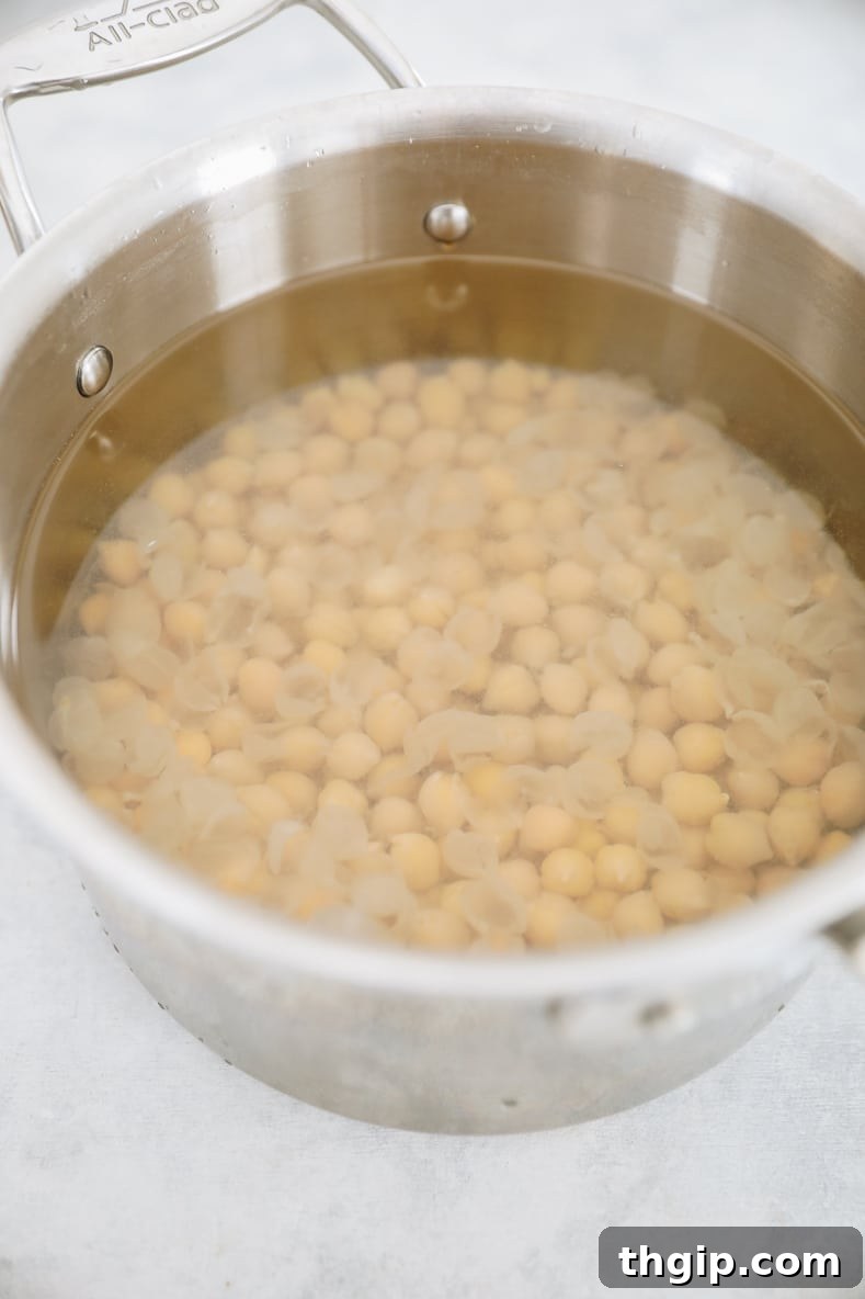 Dreamy Creamy Hummus 5 The process of removing skins from cooked chickpeas in a pot filled with cold water, illustrating the technique for achieving smooth hummus.