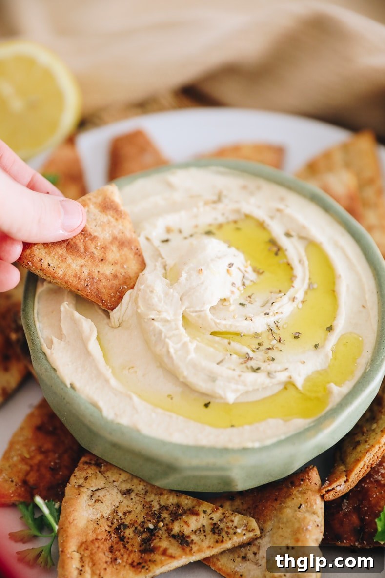 Dreamy Creamy Hummus 7 A hand gently dipping a crispy homemade pita chip into a bowl of creamy hummus, highlighting the perfect snack or appetizer.