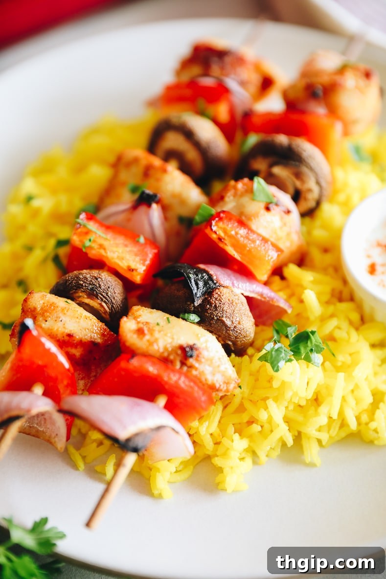 Golden Oven-Baked Chicken Skewers 7 Plated baked chicken kabobs with saffron rice and a side of yogurt sauce, garnished with parsley.