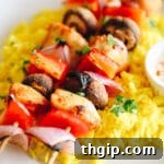 Chicken kabobs served over a bed of rice on a white plate.