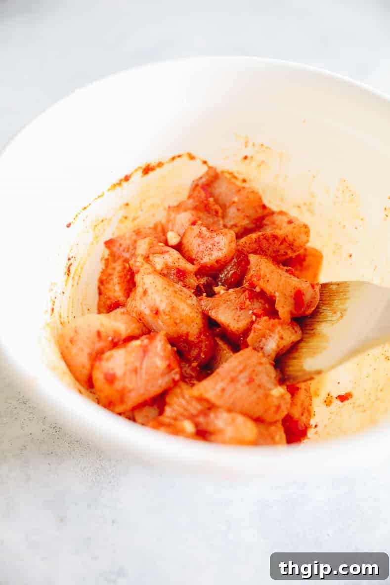 Chicken breast pieces marinating in a bowl with garlic, chili, lemon, olive oil, paprika, and salt.