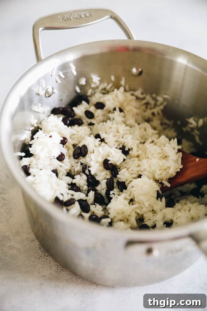 Cooked rice being combined with black beans in a pot.