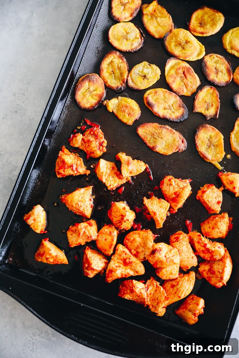 Marinated chicken and flattened plantains baking on a single sheet in the oven.