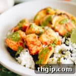 Piri piri chicken in a white bowl served with white rice, black beans and a green sauce.