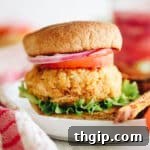 Quinoa veggie burger topped with lettuce, tomato, onion on a whole wheat bun. Burger is on a white plate and surrounded by french fries.