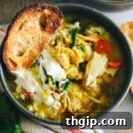 Close up of chicken lentil soup in a dark grey bowl. Soup is topped with sour cream and a piece of crunchy bread.