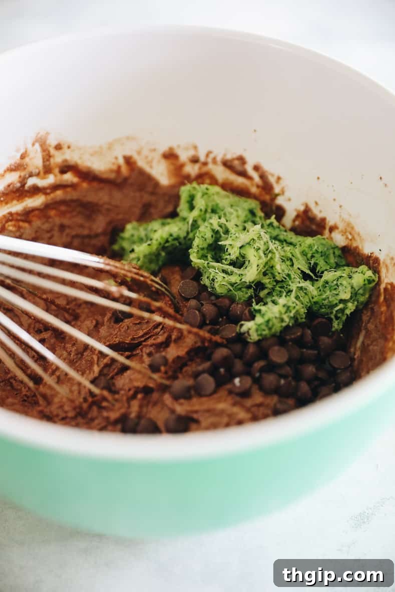 Garden Gem Chocolate Muffins 6 Wet and dry ingredients for chocolate zucchini muffins being gently mixed in a large bowl, with shredded zucchini and chocolate chips waiting to be folded in.