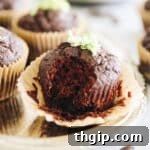 One chocolate zucchini muffin in focus with a bite taken out of it, showing its moist, dark interior.
