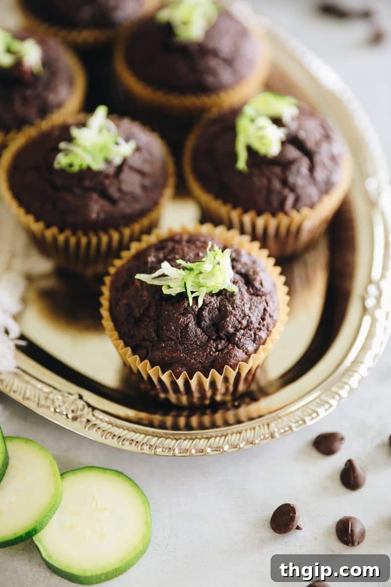 Garden Gem Chocolate Muffins 9 A stack of three golden-brown chocolate zucchini muffins on a cooling rack, with more muffins blurred in the background, highlighting their delicious texture.