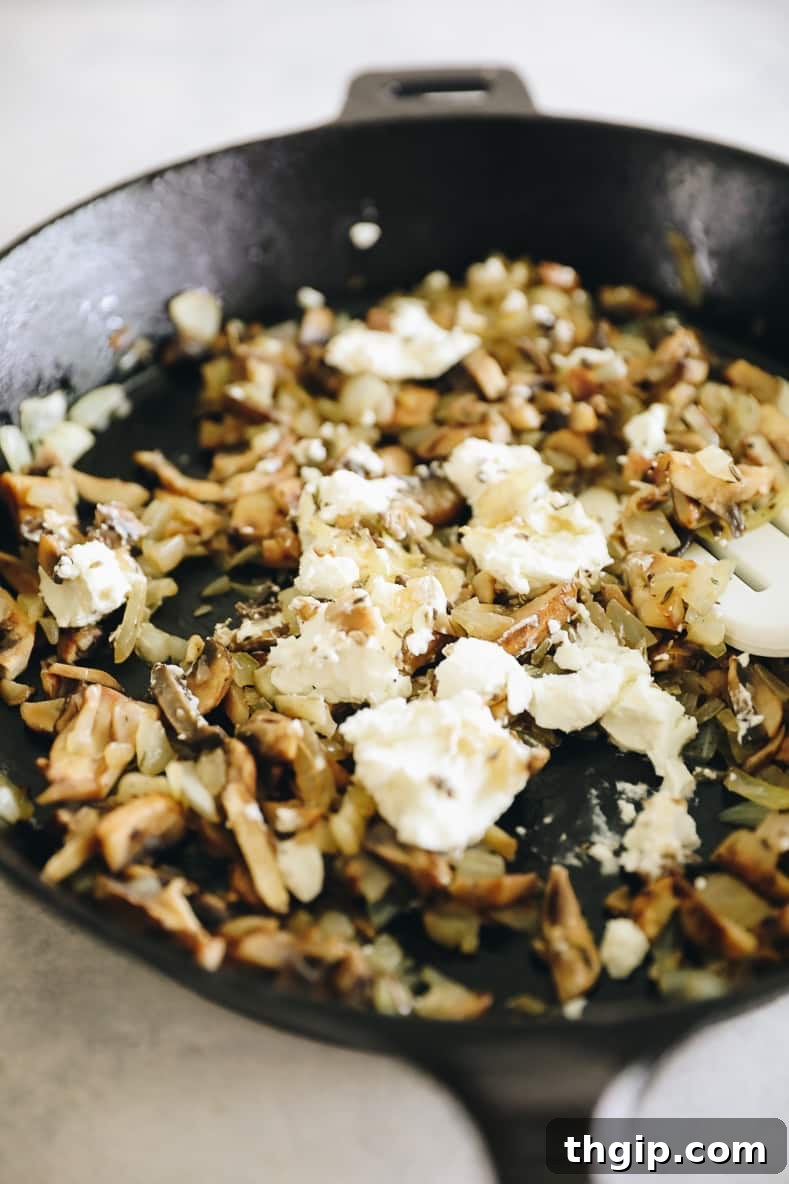 Mushroom and onion mixture with goat cheese and thyme in a skillet.