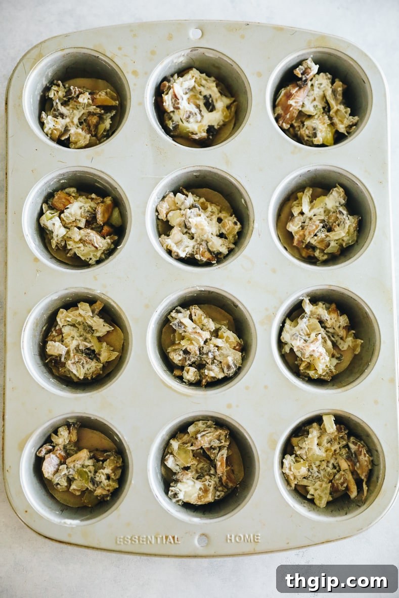 Greased muffin pan with vegetable mixture at the bottom of each cup.