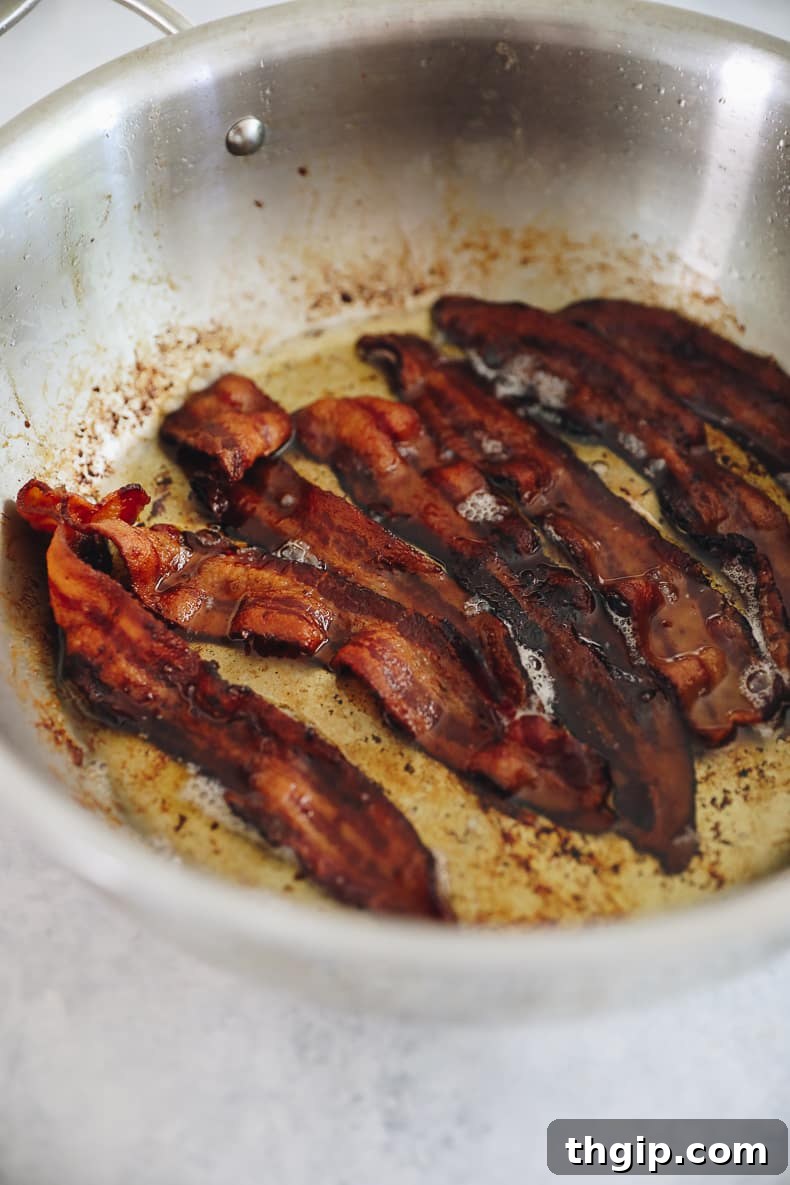 Grab-and-Go Frozen Breakfast Burritos 4 Crispy bacon strips cooking in a pan, prepared for delicious freezer breakfast burritos.